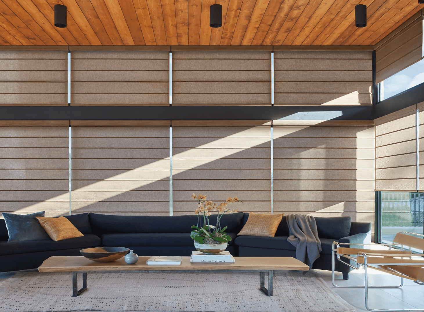 motorized-roller-shades-large-windows Large-window roller shades in a spacious living room with wood ceilings and a navy blue sectional sofa.